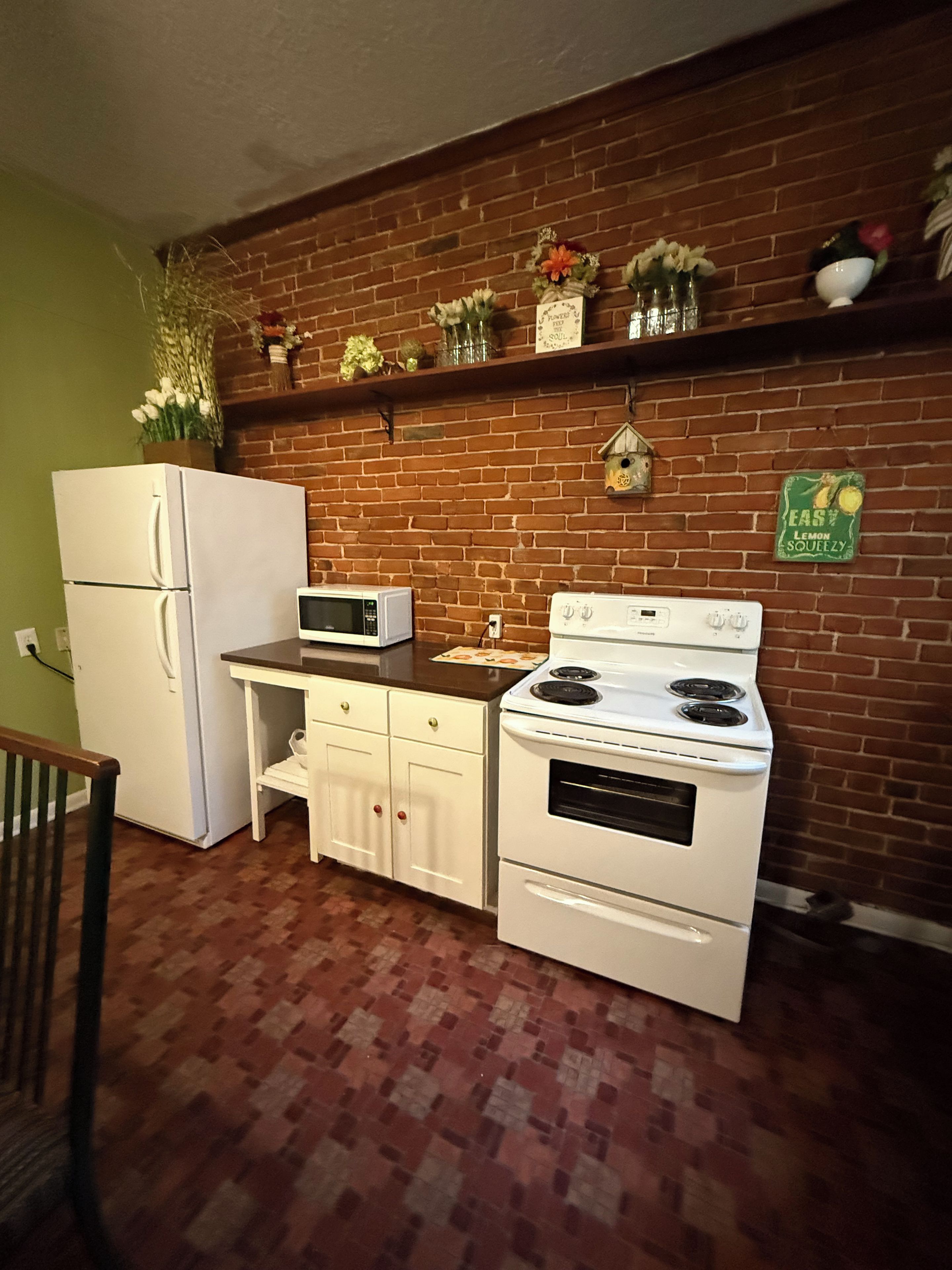 Una cocina con pared de ladrillo, electrodomésticos blancos y una estantería con adornos.