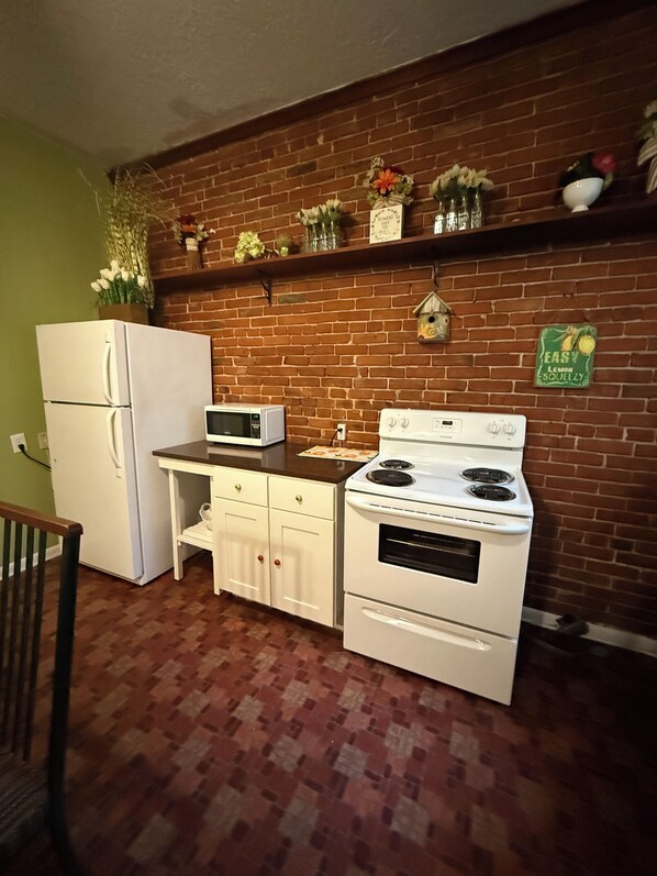 A kitchen with a brick wall, white appliances, and a shelf with decorative items.
