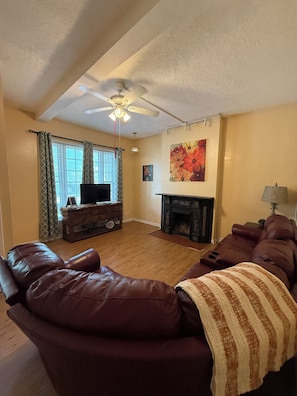 A living room with a fireplace, leather sofas, a ceiling fan, and a television. - Row House Suite 927 (Topeka)