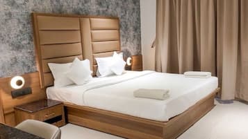 Moderni hotellihuone, jossa on puinen sänky, valkoiset vuodevaatteet, yöpöytä, työpöytä ja suuri ikkuna, jossa on verhot.