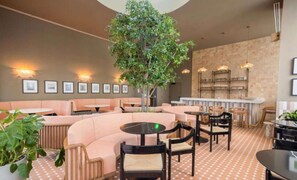 A modern lounge area with seating arrangements, a central tree, and a bar area with shelves. - The Crosby 2BR Balcony by Palermo Home (Miami)
