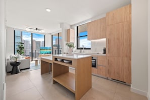 A modern kitchen with wooden cabinets, a central island, and a view of the cityscape through large windows. - The Crosby 2BR Balcony by Palermo Home (Miami)