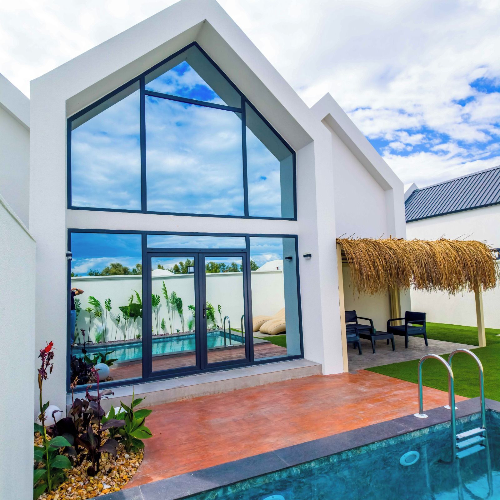 Una casa moderna con un amplio ventanal, una piscina y una estructura de techo de paja.