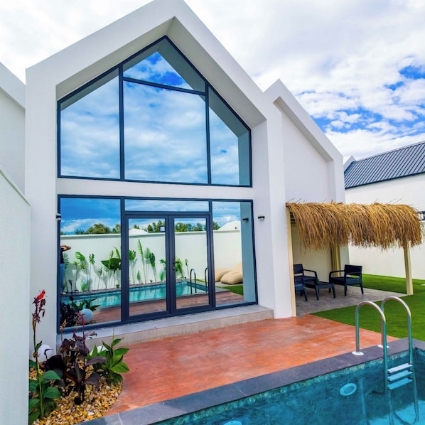 A modern house with a large glass window, a swimming pool, and a thatched roof structure.