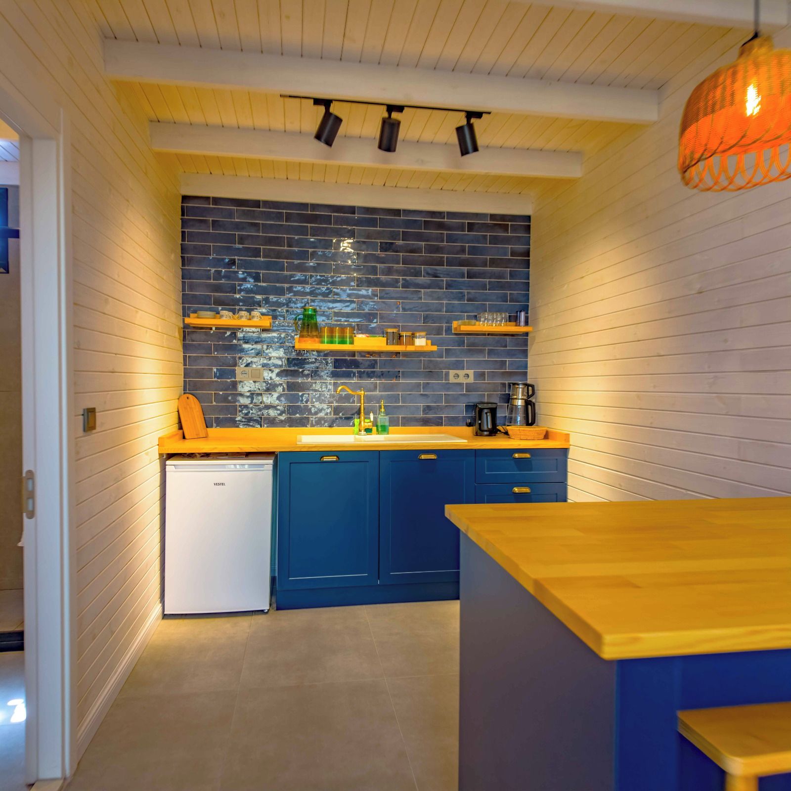 Eine kleine Küche mit blauen Schränken, einem weißen Geschirrspüler und einer Holz Arbeitsplatte.