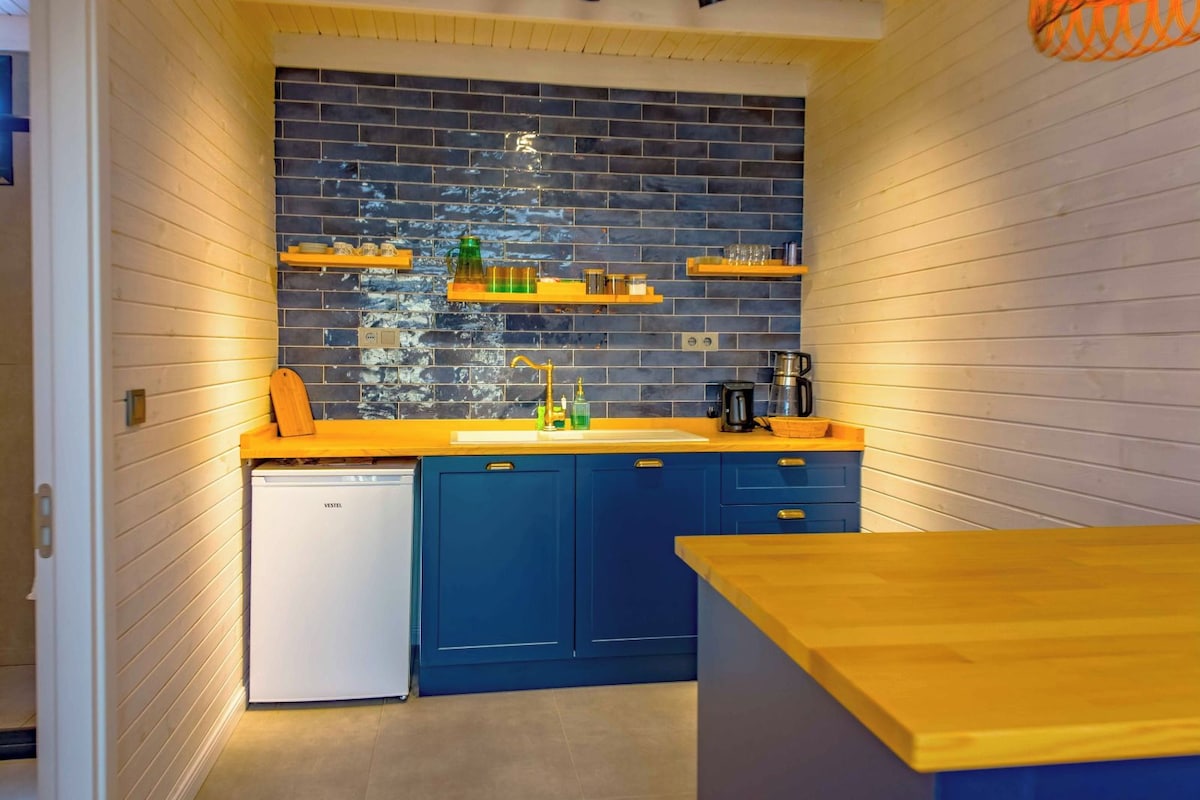 Eine kleine Küche mit blauen Schränken, einem weißen Geschirrspüler und einer Holz Arbeitsplatte.