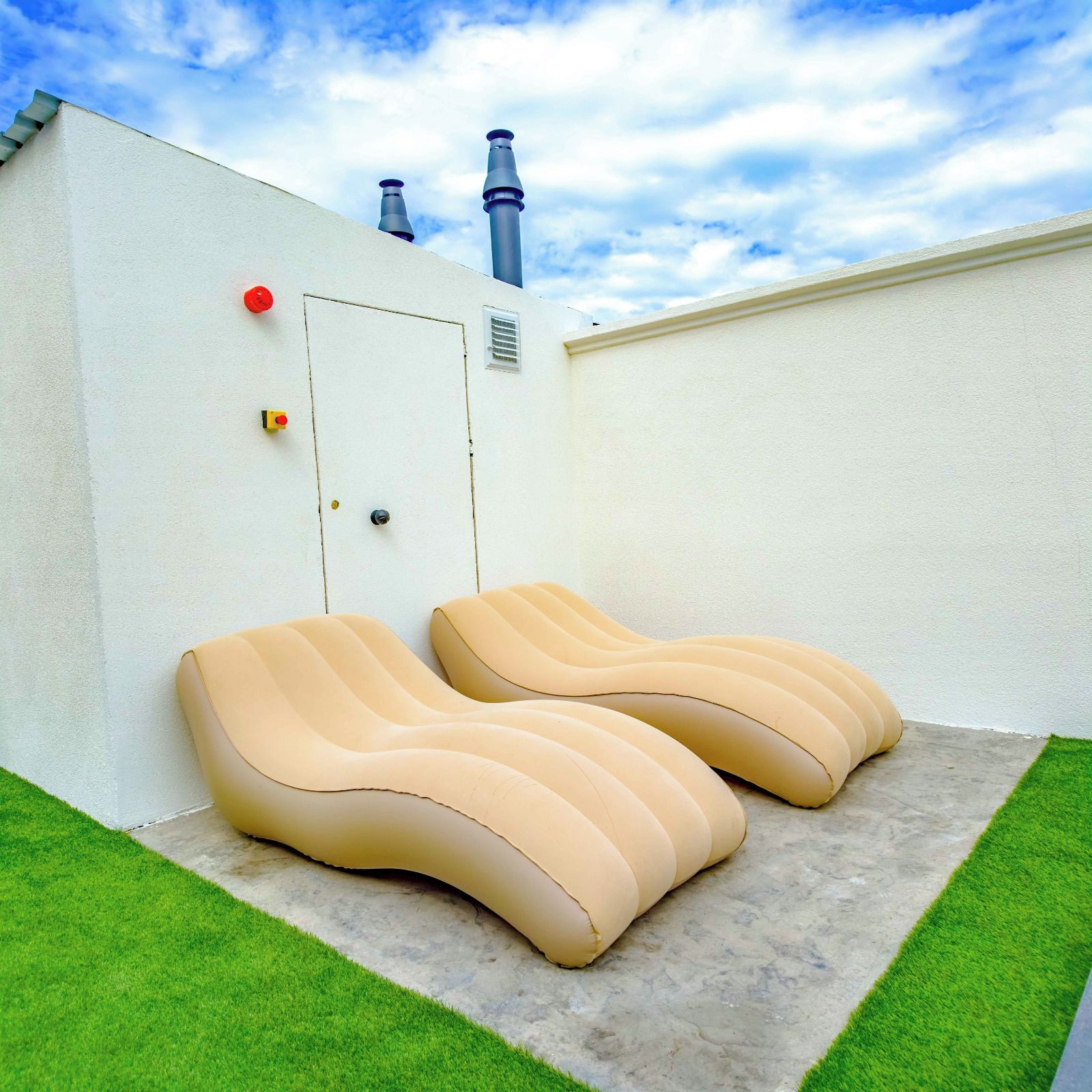 A pair of lounge chairs on a concrete patio with a white wall and a small door.