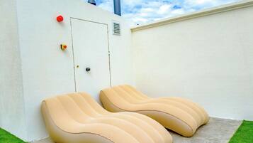 A pair of lounge chairs on a concrete patio with a white wall and a small door.