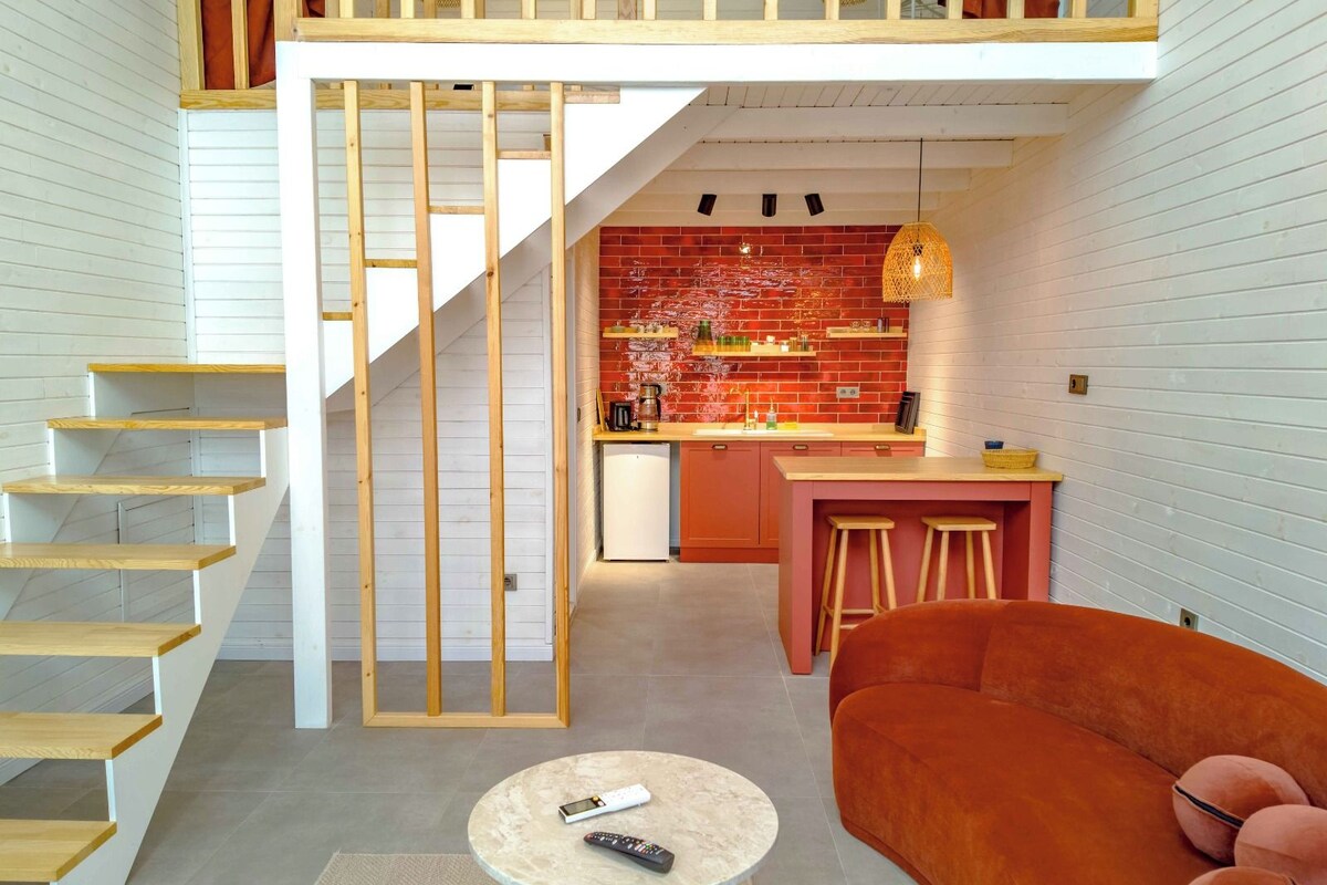 Ein modernes Interieur mit einer Treppe zu einem Schlafzimmerpodest, einer Küche mit roter Ziegelrückwand und einer gemütlichen Sitzecke mit rundem Couchtisch.