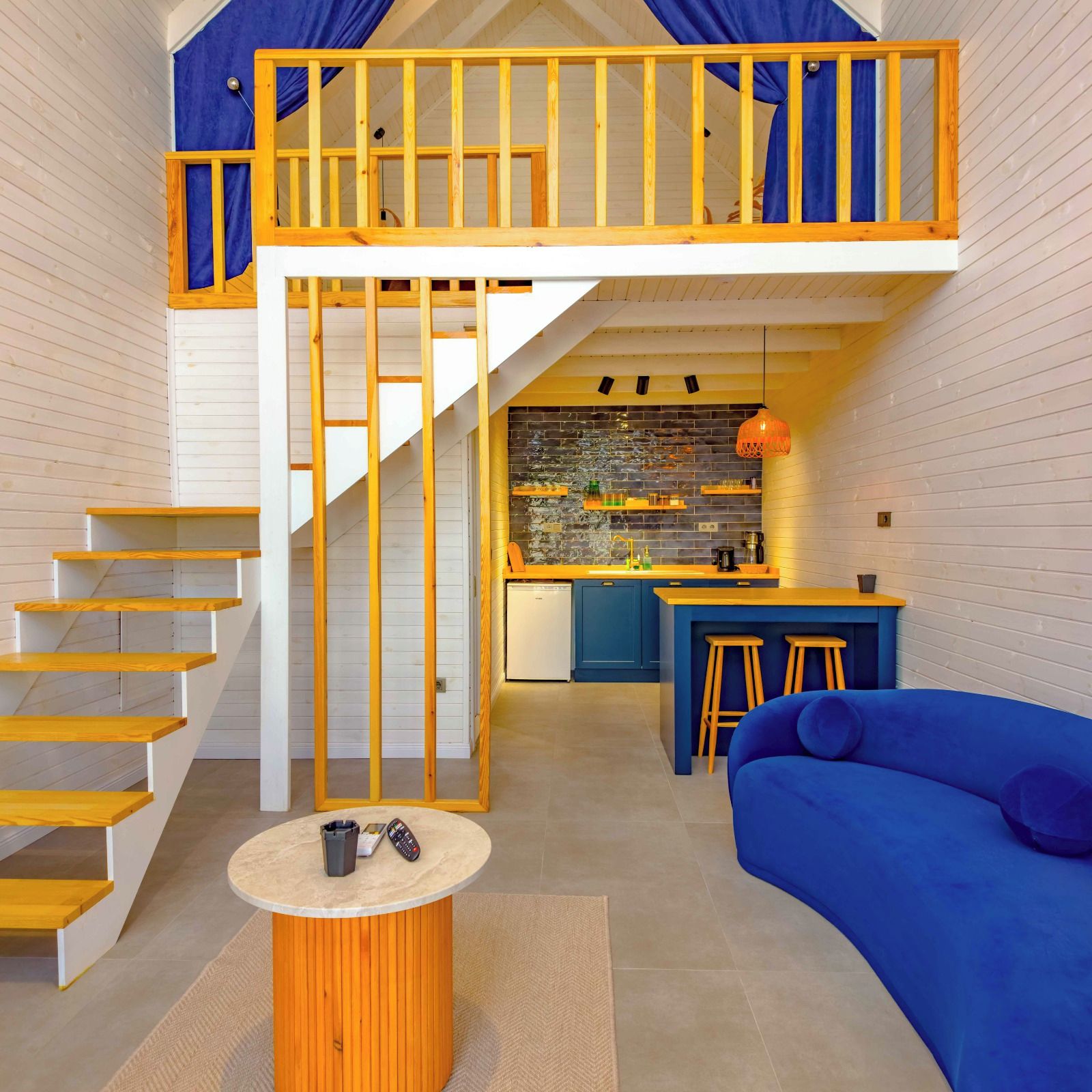 Un espace de vie moderne de style loft, avec un escalier en bois, un coin cuisine et un canapé bleu.