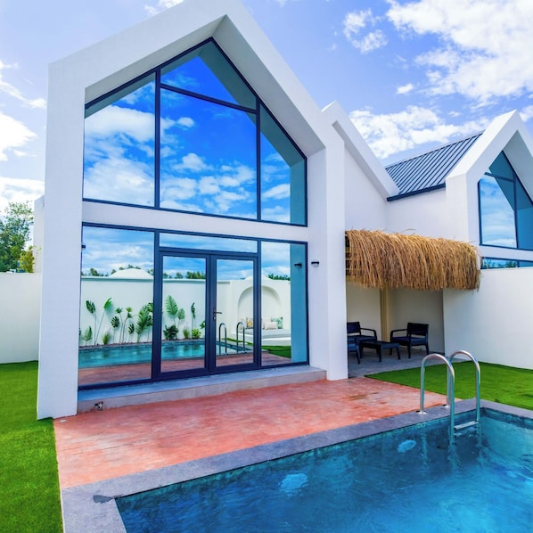 A modern house with a swimming pool, large windows, and a thatched roof.