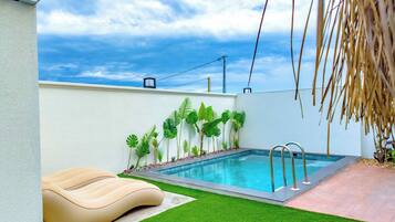 A swimming pool with a metal ladder, surrounded by artificial grass and tropical plants.