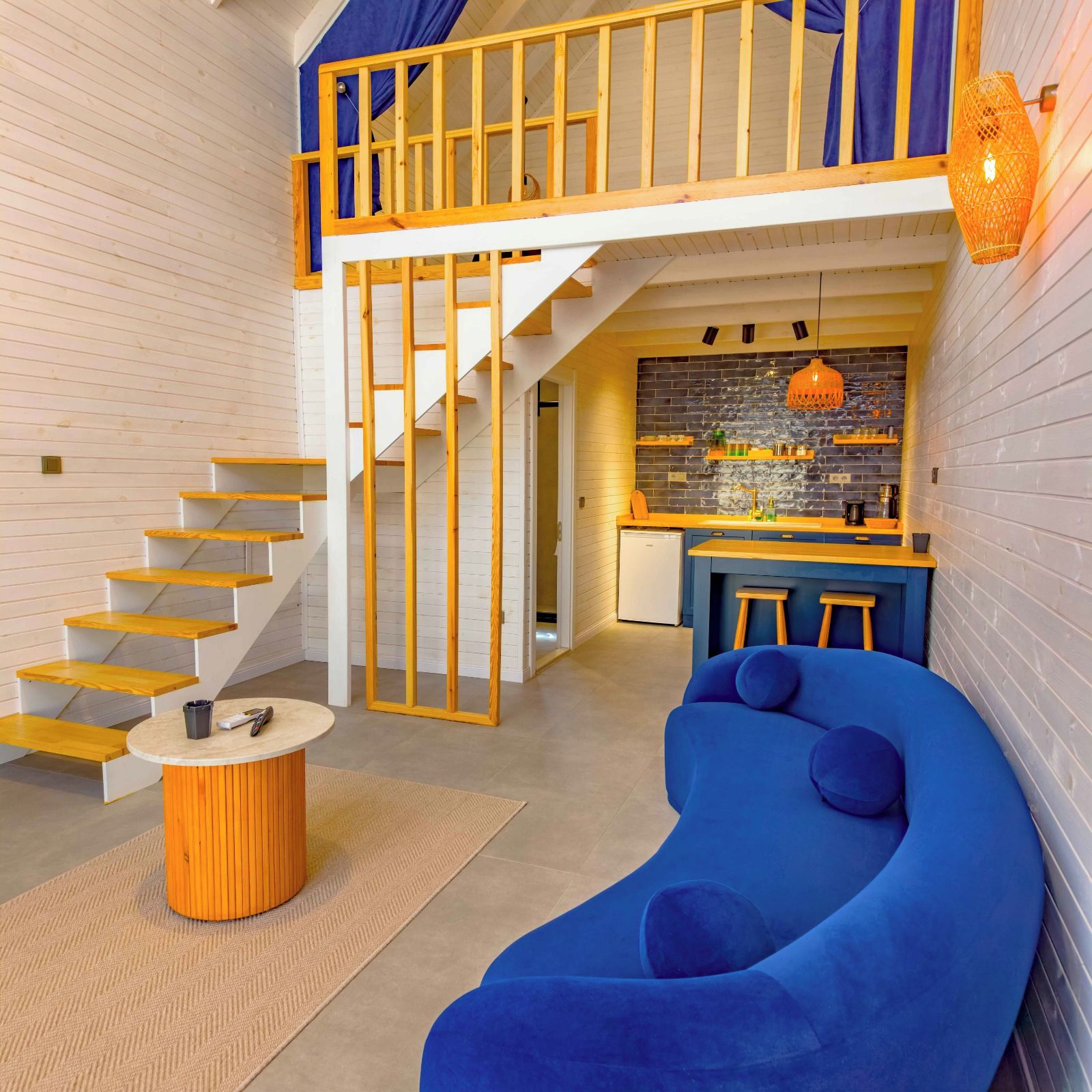 Ein modernes Interieur mit einem blauen, gebogenen Sofa, einer Holztreppe und einer Küchenzeile mit Bar.