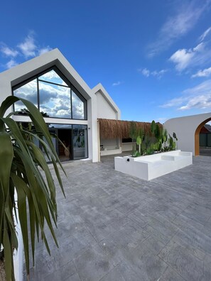 A modern building with large windows, a flat roof, and a courtyard with a thatched roof and plants.