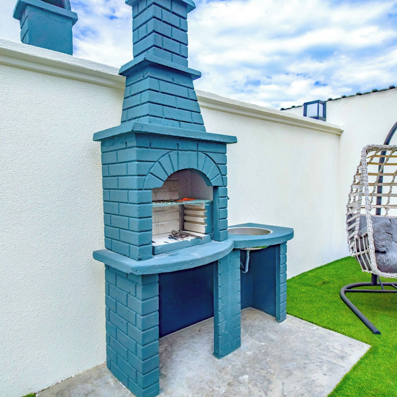Ein blauer Outdoor-Ziegelofen mit Schornstein, ein Spülbecken und ein Hängesessel.