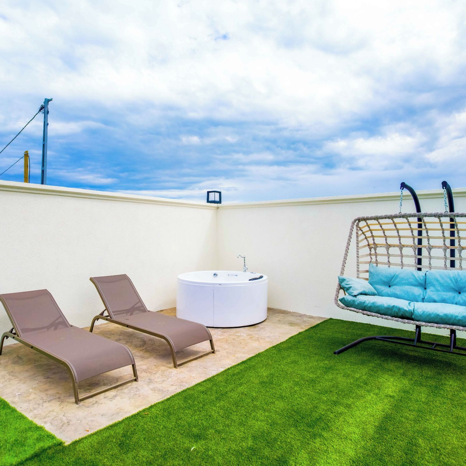 Terraço no telhado com duas poltronas de descanso, uma banheira de hidromassagem circular e uma cadeira balanço suspensa.