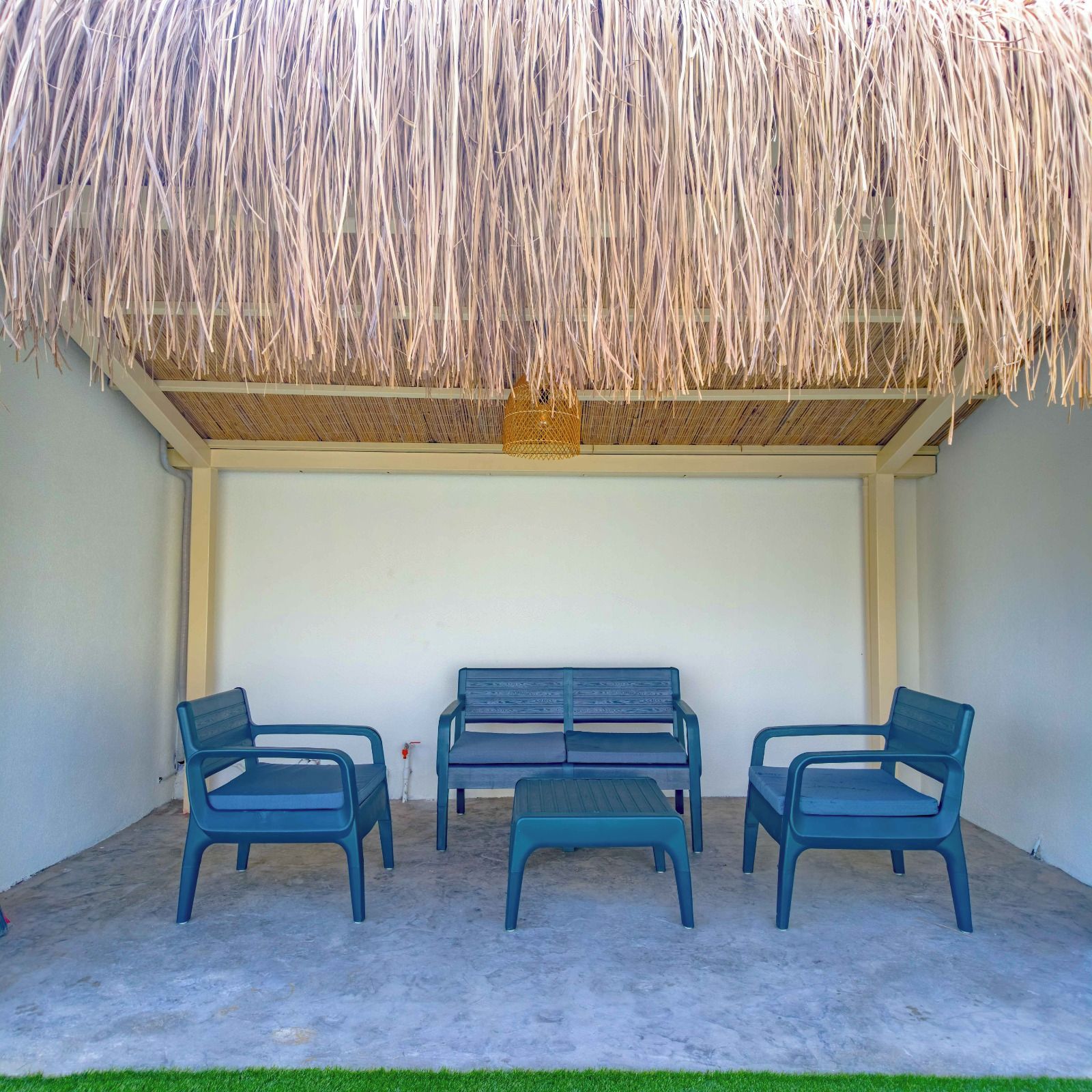 Un espacio de estar al aire libre techado, con techo de paja, un banco y dos sillas.