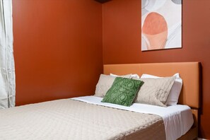 A single bed with a headboard, white bedding, and two pillows, one green and one beige, in a room with orange walls. - Comfy 2 Bedroom - Games - 1 Garage Spot - Sleeps 6 (Chicago)