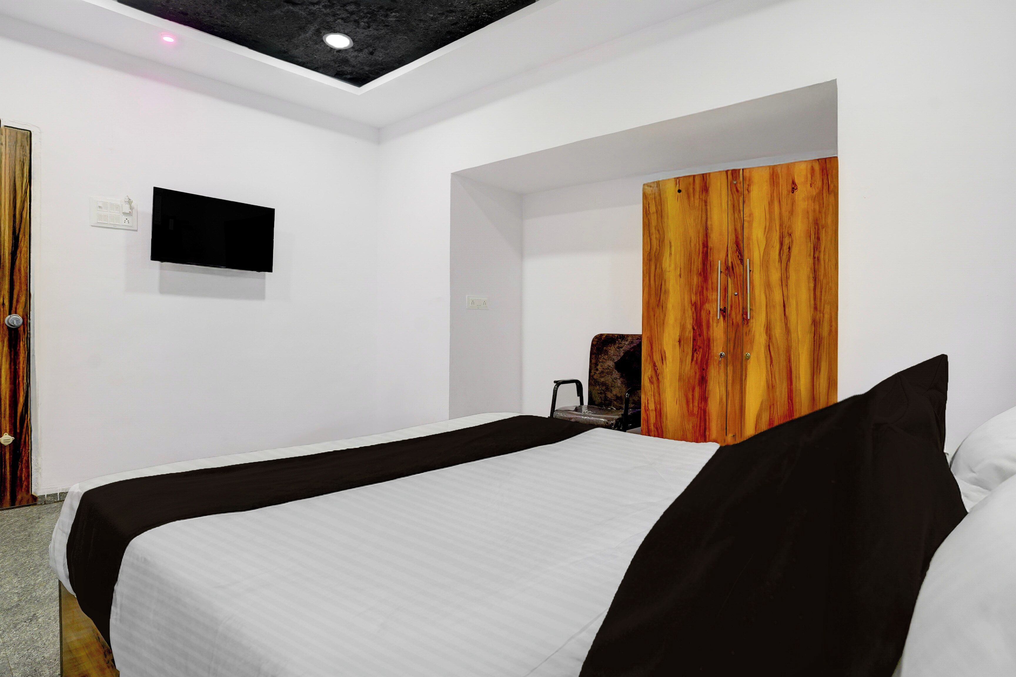 A hotel room with a bed, a television mounted on the wall, and a wooden wardrobe.