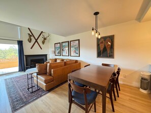 A spacious living area with a sofa, a dining table, and chairs. There is a fireplace, a ceiling light fixture, and framed pictures on the wall. - Northern Oasis near Nub's Nob (Pleasantview Township)