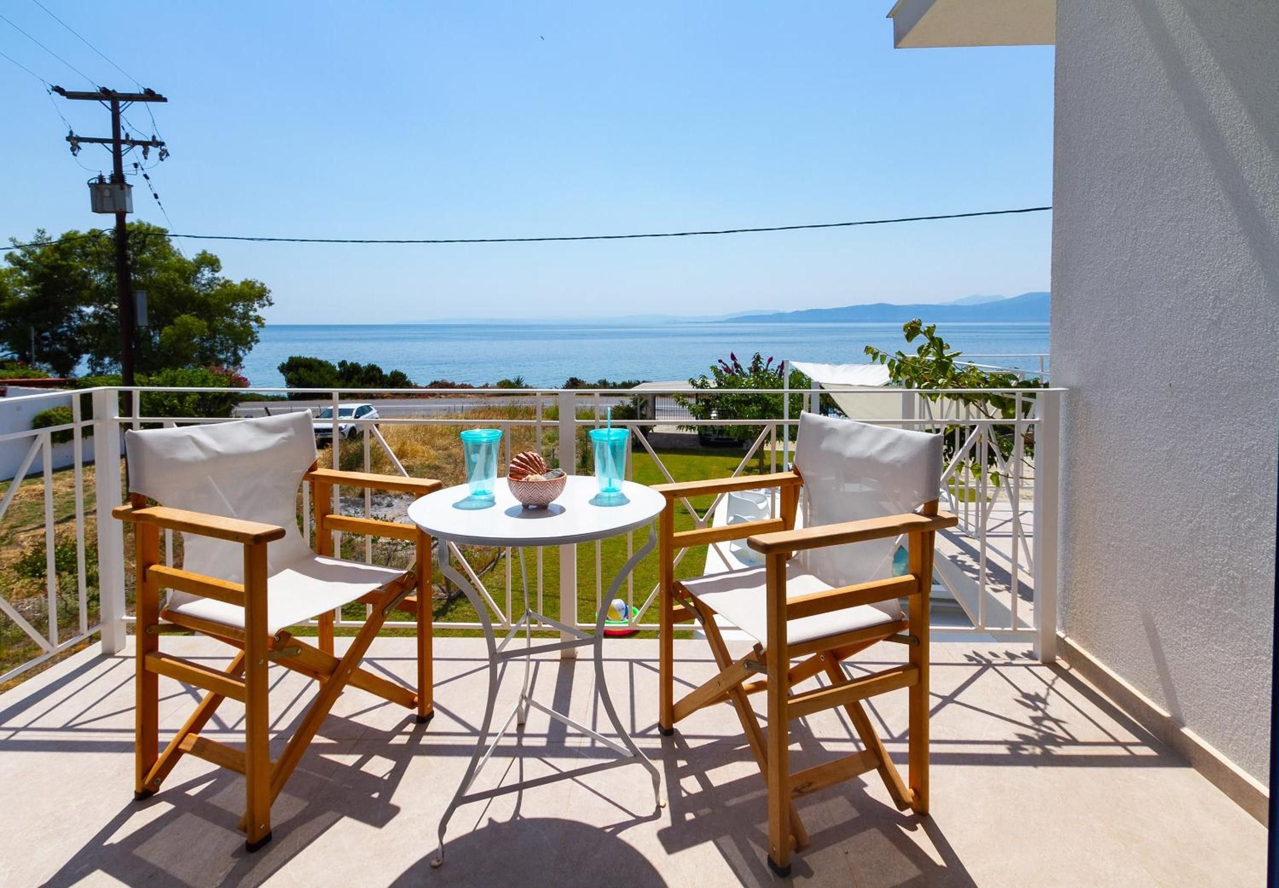 A balcony with two wooden chairs and a small round table, overlooking a body of water and distant land.