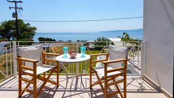 A balcony with two wooden chairs and a small round table, overlooking a body of water and distant land.
