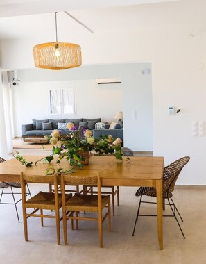 Een eetruimte met een houten tafel, geweven stoelen en een hanglamp.