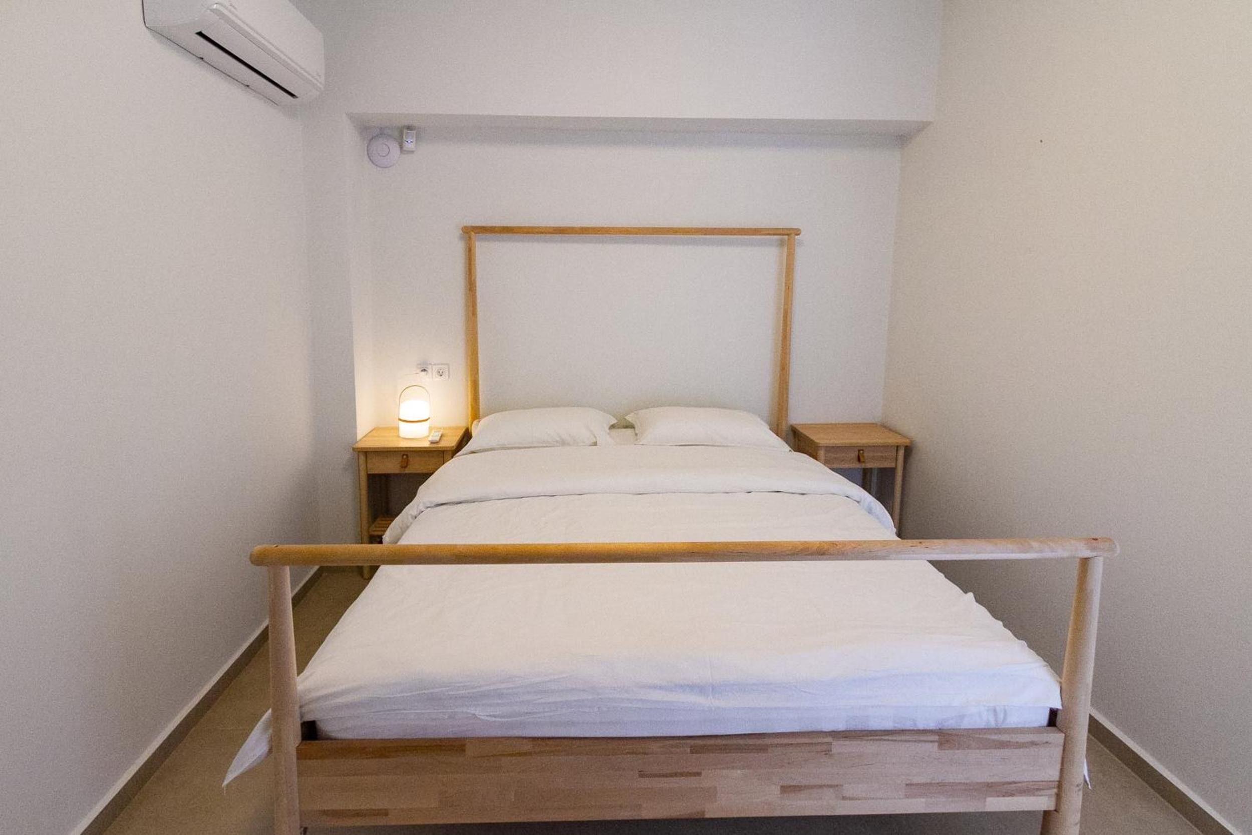 A single bed with a wooden frame, two bedside tables, and a wall-mounted air conditioning unit.
