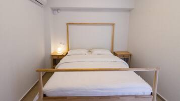 A single bed with a wooden frame, two bedside tables, and a wall-mounted air conditioning unit.