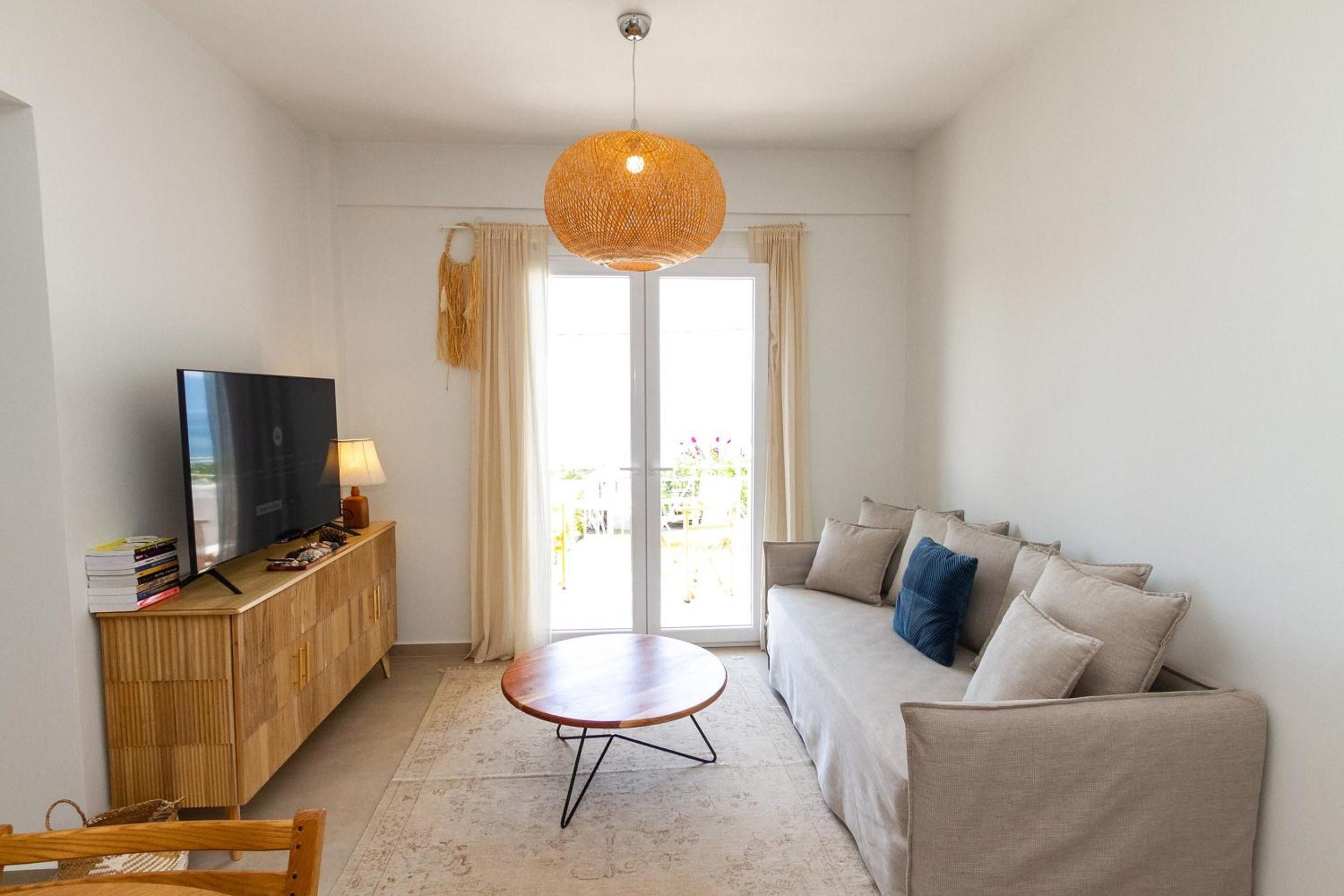 A living room with a sofa, a coffee table, a TV on a wooden cabinet, and a hanging light fixture.