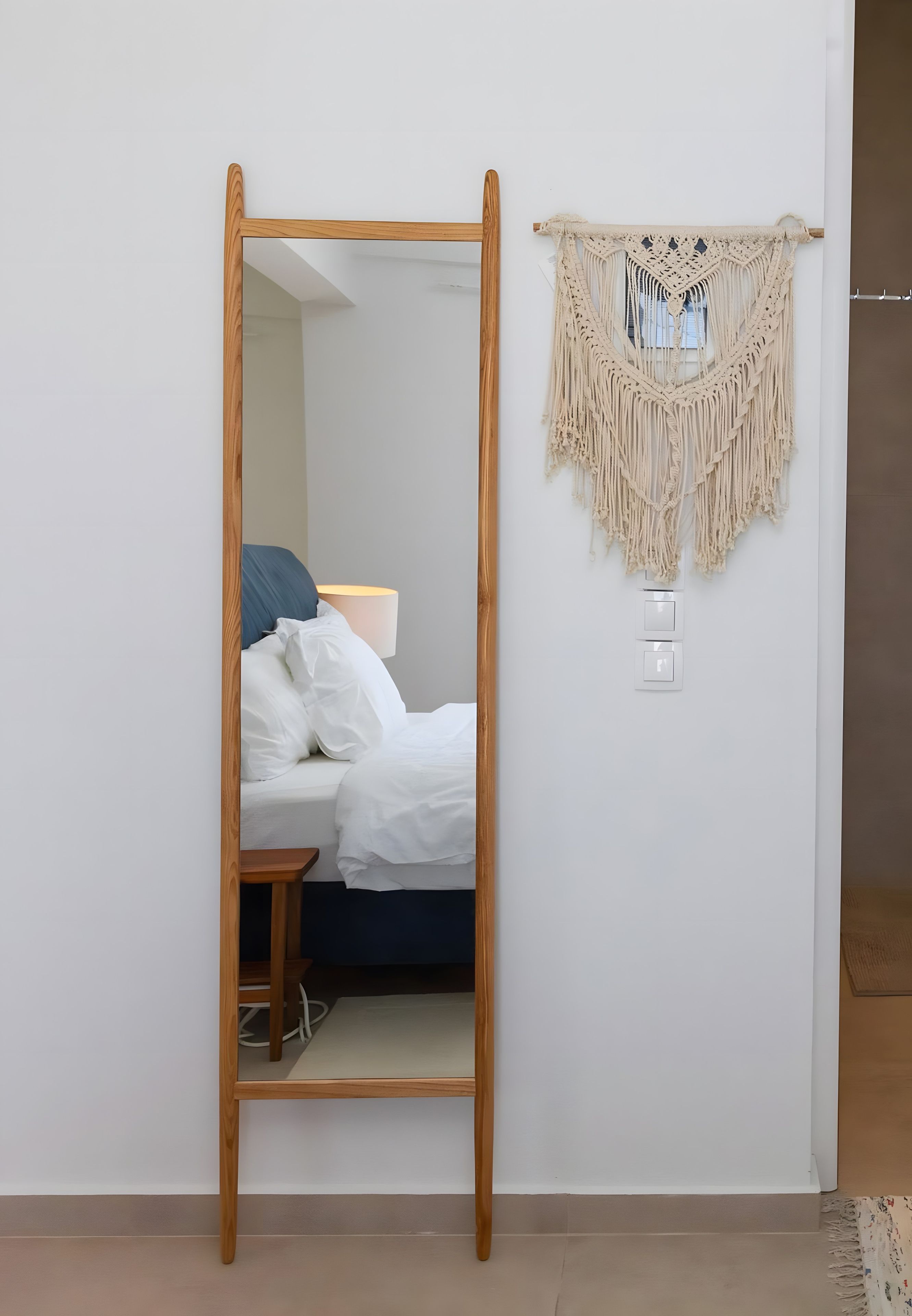 A room with a bed, a wooden-framed mirror, and a macramé wall hanging.