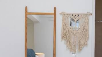 A room with a bed, a wooden-framed mirror, and a macramé wall hanging.