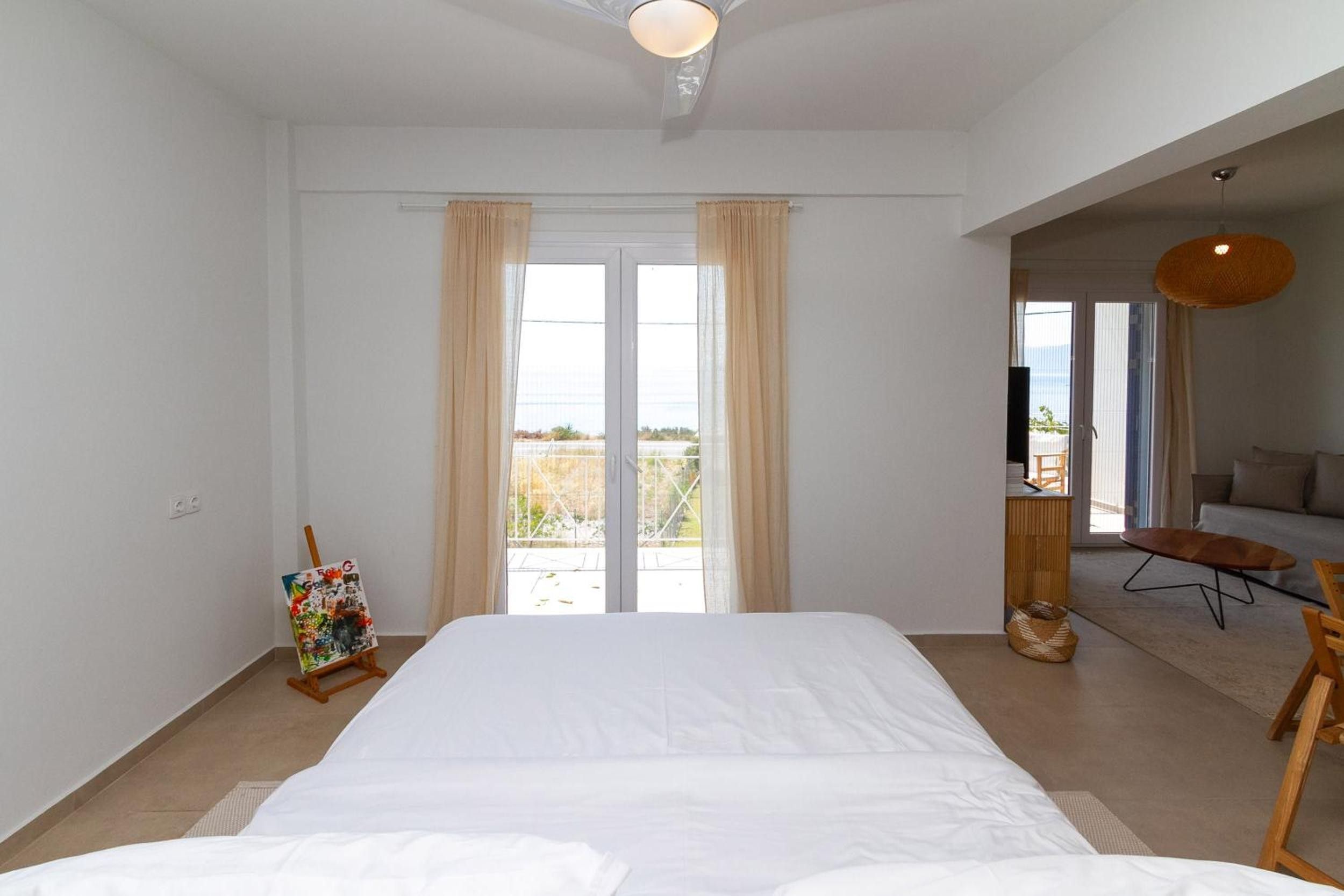 A spacious bedroom with a large bed, a painting on the wall, and a view through the window.