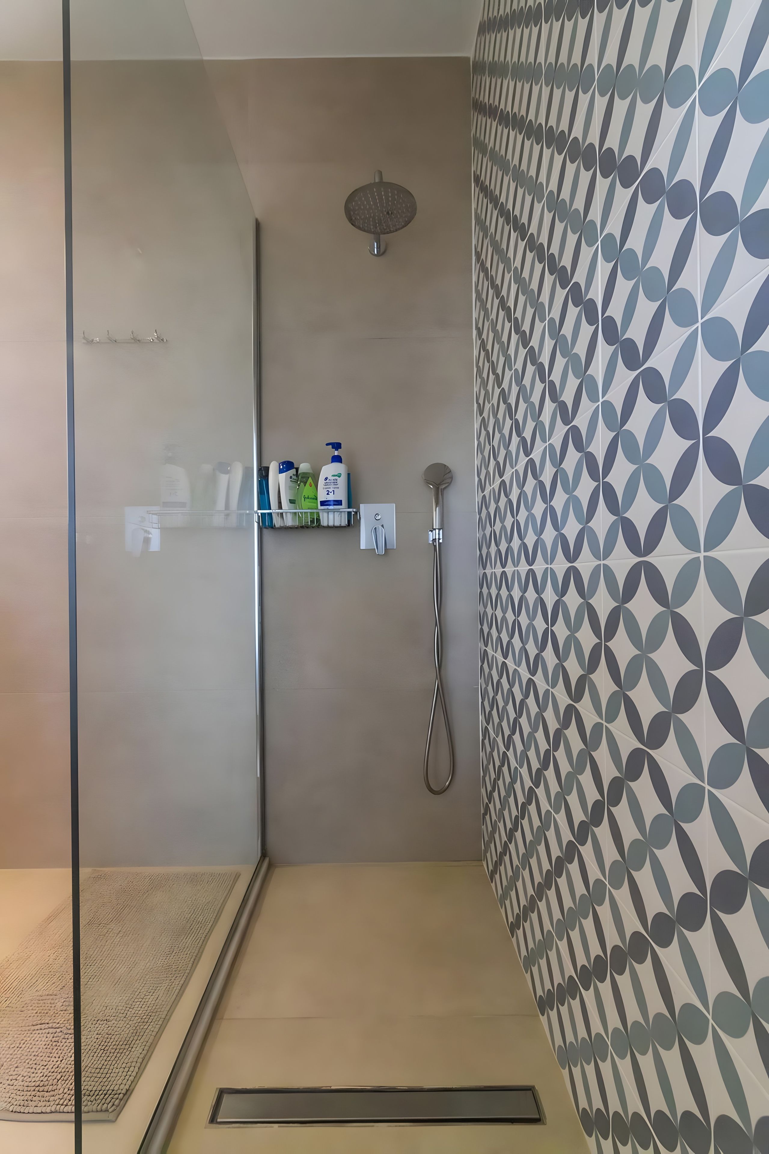 Un espacio de ducha moderno con puerta de vidrio, cabezal de ducha de mano y repisa con artículos de tocador.