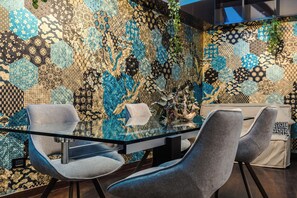 A modern interior with a glass table surrounded by grey upholstered chairs, set against a wall with a complex mosaic pattern. - New Listing (Roma)