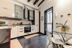 A modern kitchen with a built-in oven, a coffee machine, and a glass dining table with chairs. - New Listing (Roma)