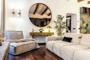 A living room with a round mirror, a sofa, a chair, a small table with a lamp, and a potted plant. - New Listing (Roma)