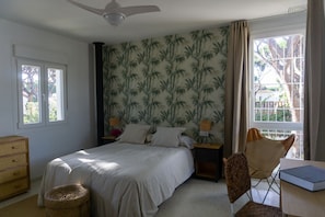 Quarto com cama, duas mesas de cabeceira, uma cadeira, escrivaninha, janela e ventilador de teto.