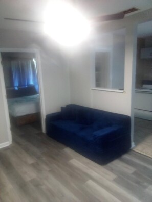 Habitació amb un sofà blau, un llit amb capçalera blava i una paret blanca.