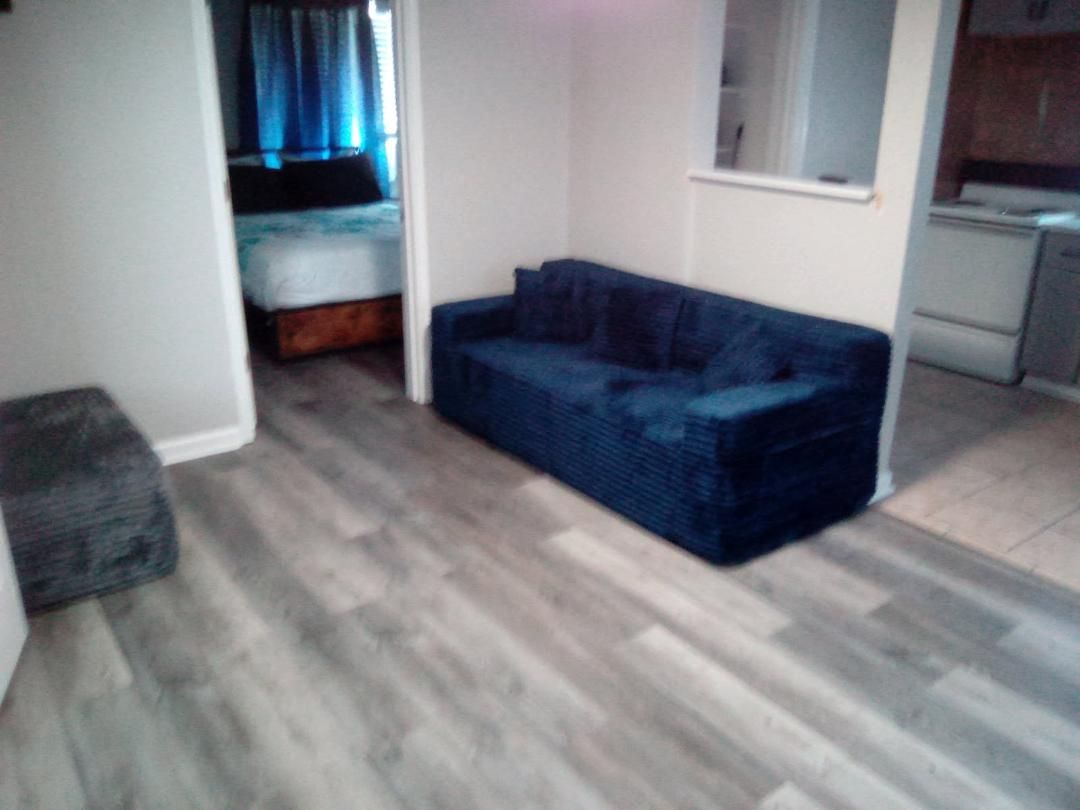 A room with a blue sofa, a bed with a blue headboard, and a small kitchen area.