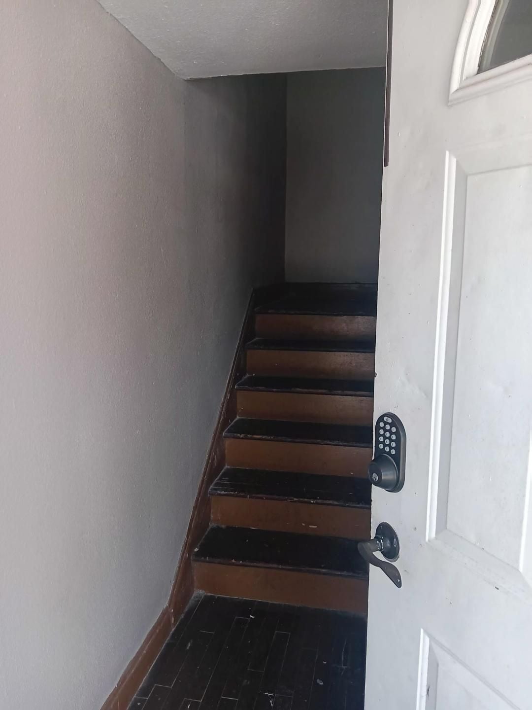 A staircase with wooden steps leading to a white door with a keypad lock.