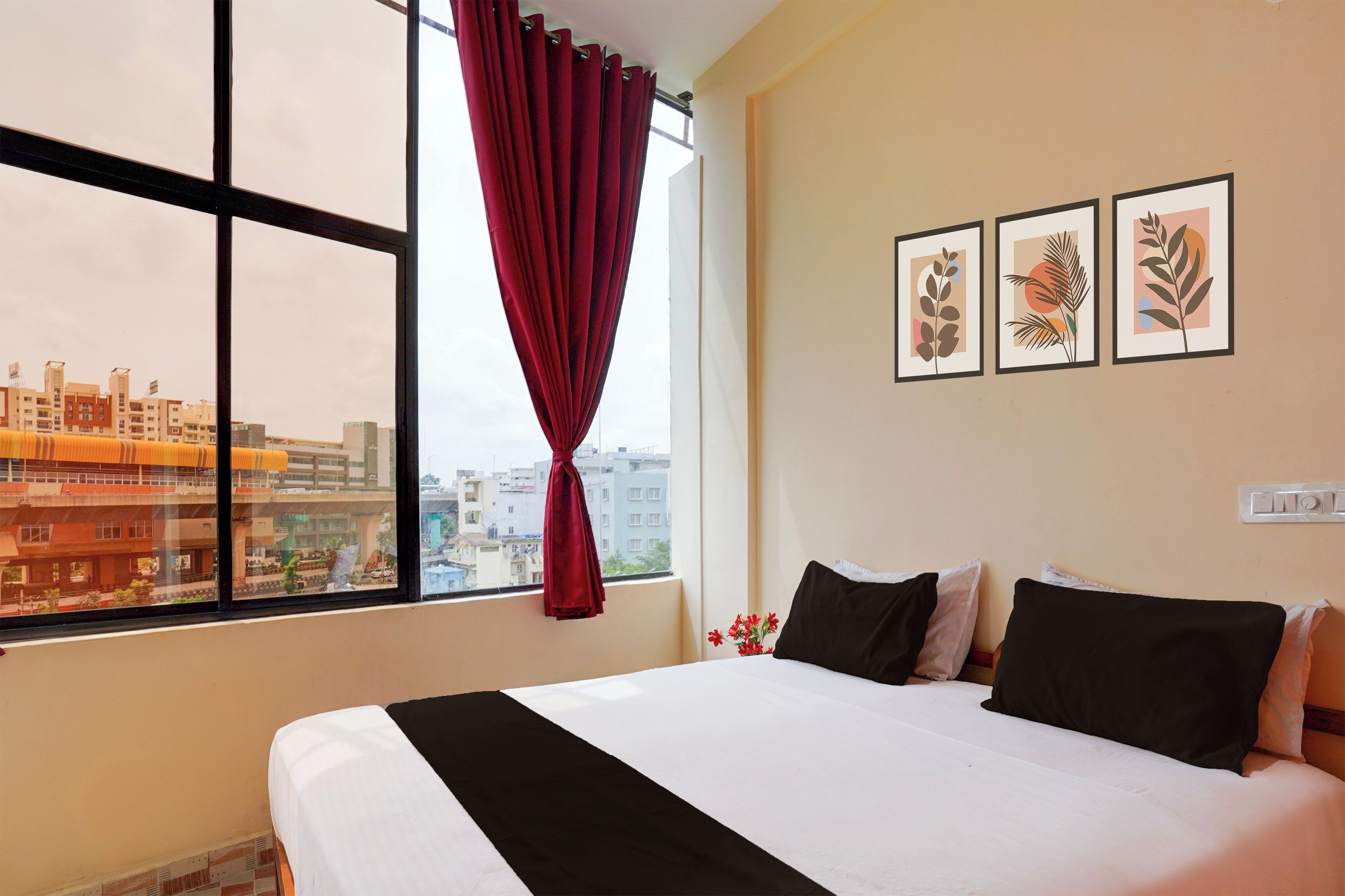 A hotel room with a large window, a bed with black and white bedding, and three framed botanical prints on the wall.