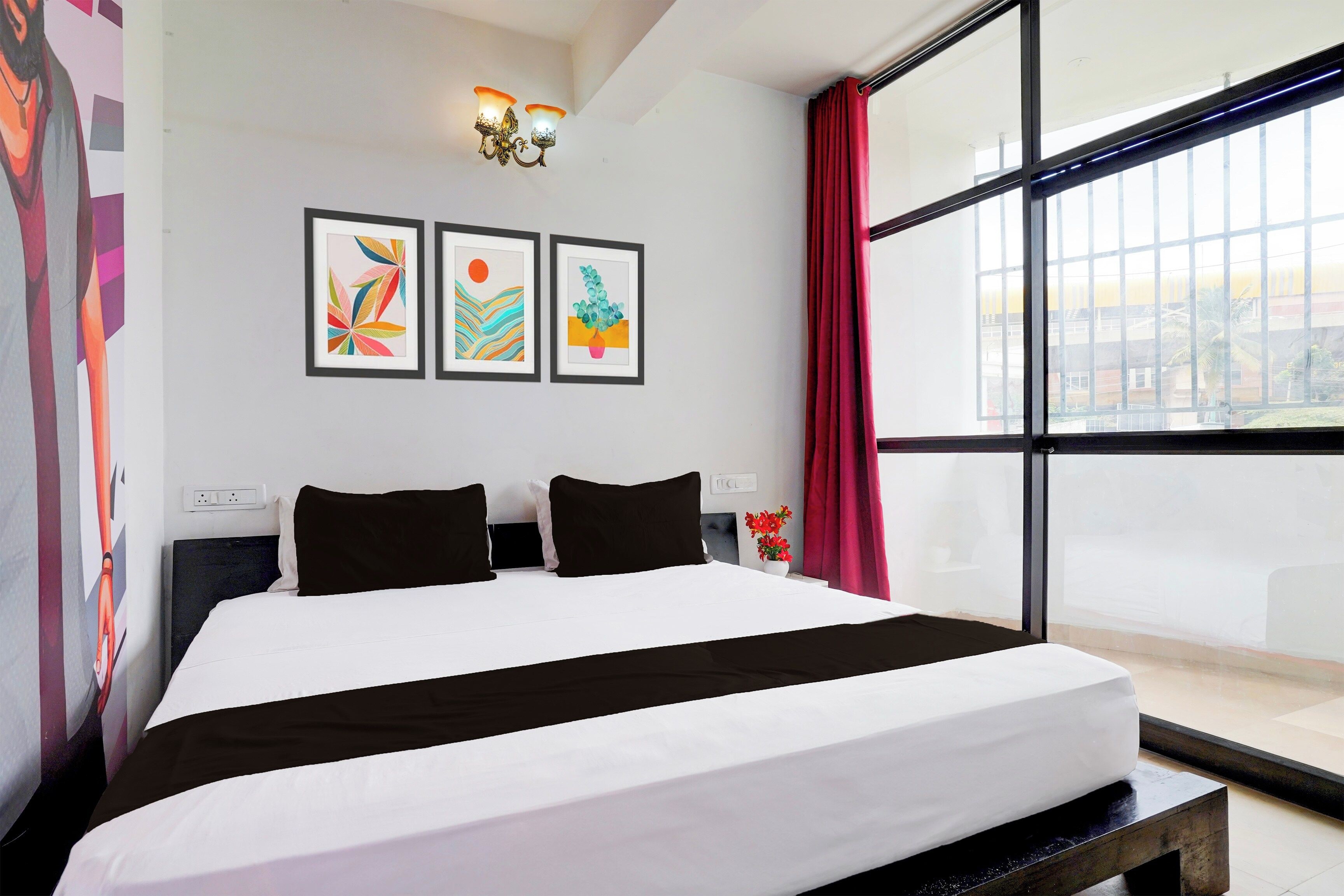 Quarto de hotel com uma cama grande, vista para a cidade e três quadros na parede.