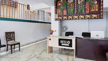 Ein Hotel-Empfangsbereich mit Marmorboden, einem Holzbüro, einem Sessel, einem Wanddekor und einem Balkon mit Geländer.