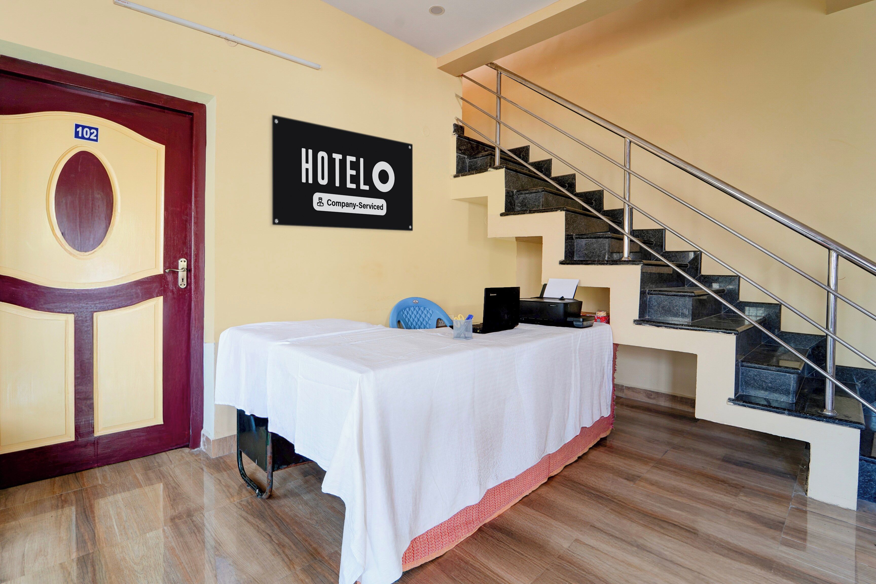 Habitación de hotel con cama, escritorio con computadora, escalera y puerta con el número 102.