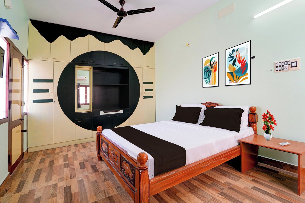 Un dormitorio con cama, mesita de noche, televisor de pared y dos cuadros enmarcados.