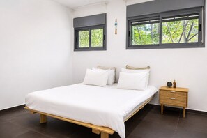 A bedroom with a bed, two windows, a bedside table, and a nightstand. - Garden View Apt • Near the Beach by SeaNRent (Tel Aviv-Yafo)