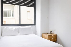 A bedroom with a bed, a window, and a wooden nightstand. - Garden View Apt • Near the Beach by SeaNRent (Tel Aviv-Yafo)