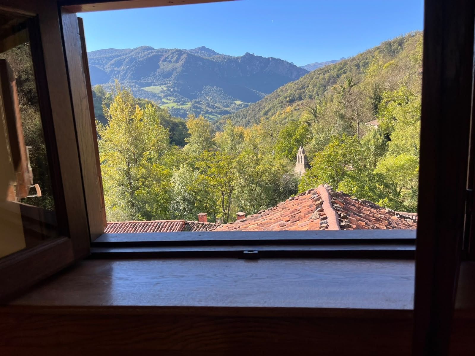 A window with a view of a mountainous landscape, a tiled roof, and a wooden structure.