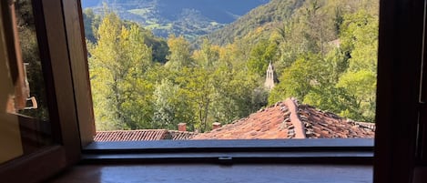A window with a view of a mountainous landscape, a tiled roof, and a wooden structure.